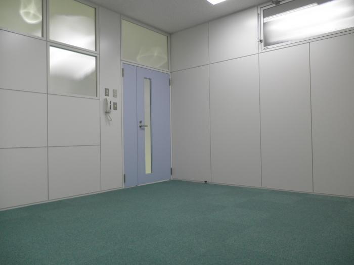 白い壁と緑色のカーペットに薄い青のドアがある業務室の写真