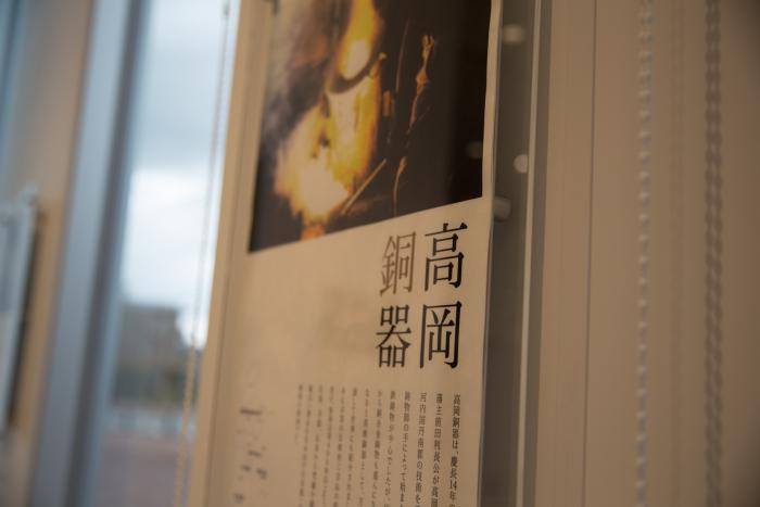 「高岡銅器」と大きく書かれ、銅器を制作している様子の写真と説明が書かれている展示プレートの写真
