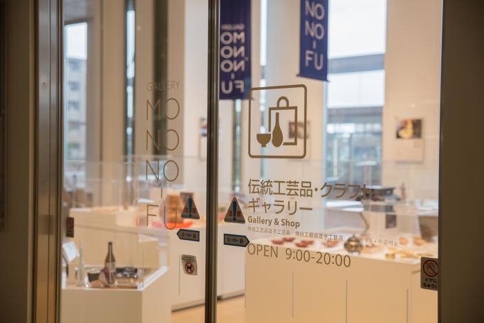 白い壁とぬくもりのある肌色の床の部屋にショーケースの上にいくつも伝統工芸品やクラフト品がきれいに展示されている様子の伝統工芸品・クラフトギャラリー入り口の写真
