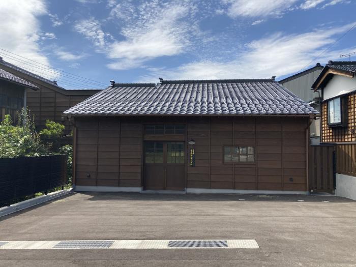 瓦屋根にこげ茶の壁が特徴的な木造平屋の横長の建物の写真