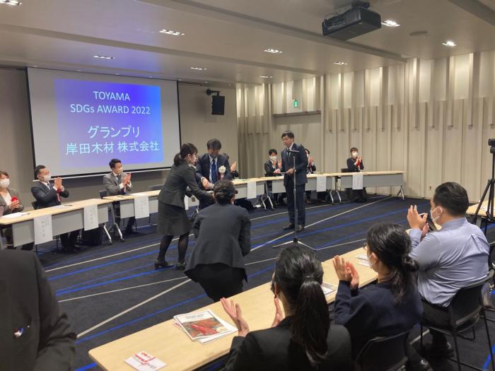二列に並べられた机の間で、表彰式が行われ、机の前に座った参加者たちが拍手をしている写真