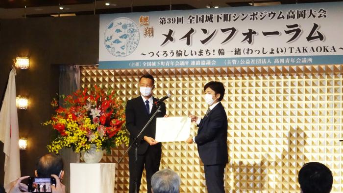 横田建具・木工の横田誠二さんと1人の男性が、2人で賞状を持って立っている様子を写した写真