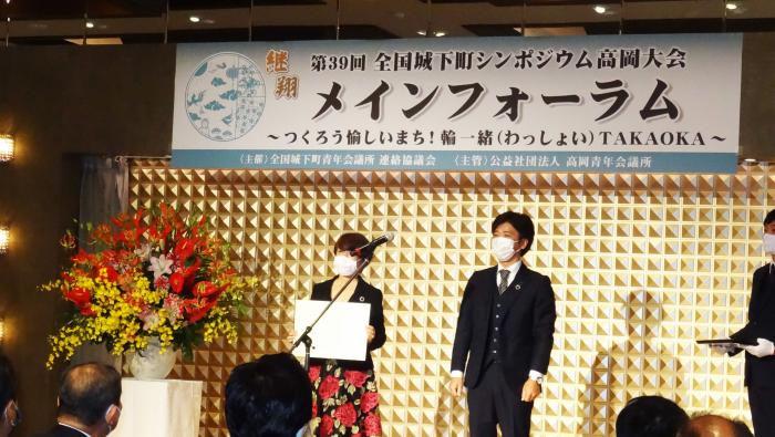 ウーマンワンダーラボの荒井里江さんと1人の人が壇上に立ち、荒井里江さんが賞状を手にしている様子を写した写真