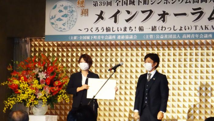 株式会社能作の能作千春さんと1人の人が壇上に立ち、能作千春さんが賞状を手にしている様子を写した写真