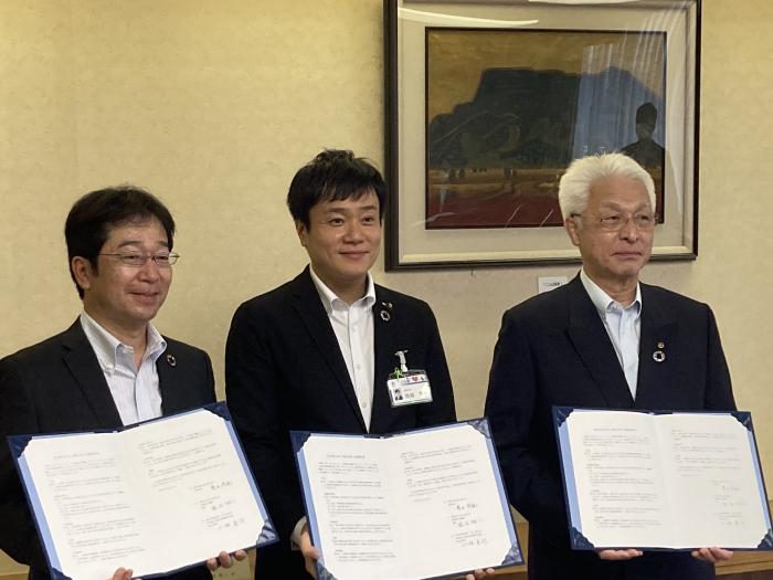 高岡市役所庁議室内で、高岡市長、高岡商工会議所の代表者、東京海上日動の代表者の男性3名が並び立ち協定書を胸の高さで掲げている様子の写真