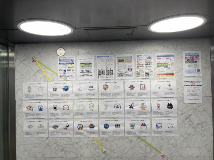建物のエントランスの壁に、「たかおかSDGsロゴ応募作品」のコピーが貼られているのを、正面から見た写真