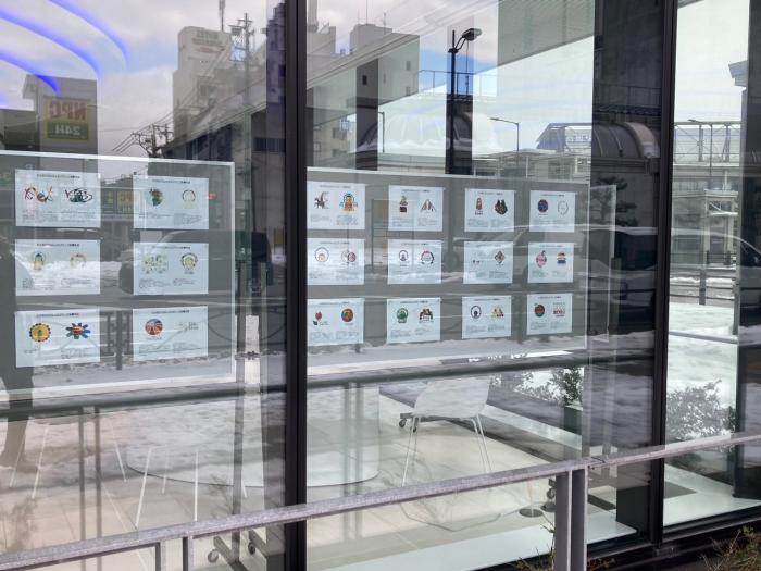 銀行らしい建物の中の衝立に、「たかおかSDGsロゴマーク」応募作品のコピーが貼られているのを、外からガラス越しに見た写真