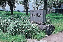 「木舟城跡」と書かれた石碑と草原があり、奥に和風の建物がある様子の写真