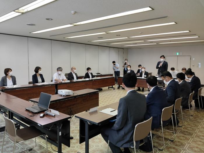 懇談会の写真。四角に並べられた机に参加者が座っており、それを撮影している人もいる。