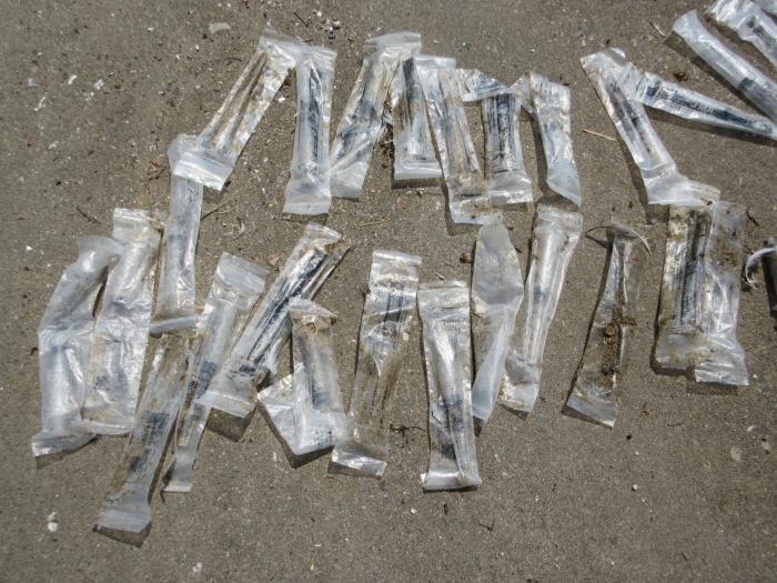 海岸に大量に漂着した、プラスチック袋入りの注射器の写真