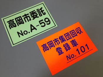 高岡市委託と書かれた緑のマグネットと高岡市集団回収登録車と書かれた赤いマグネットの写真