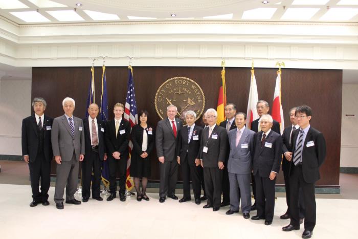 各国の国旗を背後にスーツを着た人々が並んでいる写真
