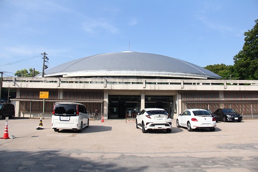 4台の車が止まっている駐車場の先にある平たいドーム状の建物の写真