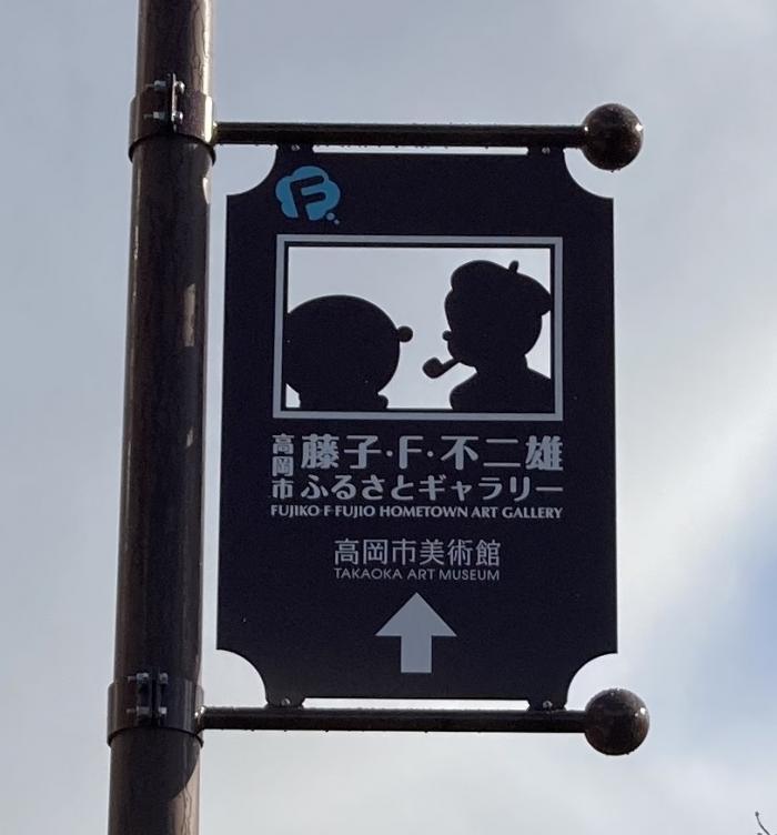 案内看板の拡大写真。看板中央の切り抜かれた空間の中に、対面するドラえもんと藤子・F・不二雄氏のシルエットが形作られている様が確認出来る