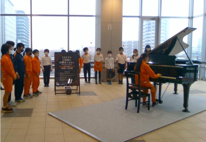 後方右側よりやや離れて撮影された、高陵小学校生徒によるピアノの演奏風景の写真