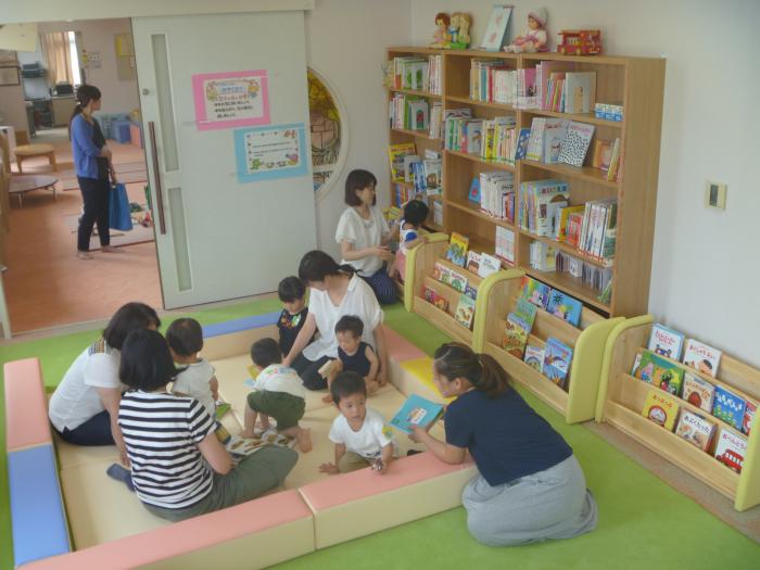絵本を読んでいる幼児と、それを支える大人たちを斜め上から写した「たっち絵本ひろば」の全景写真