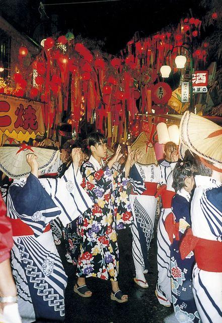 大勢の笠を被った浴衣の女性が赤い飾りの下を歩いている写真
