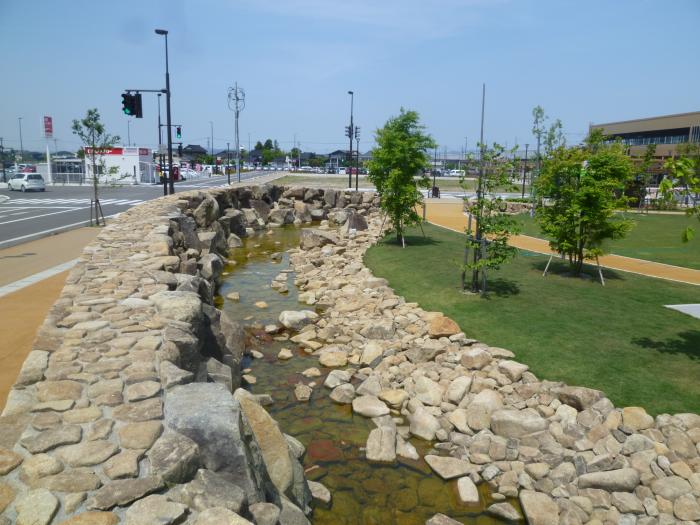 石垣の間を流れる川を中心に舗装十字道路と等間隔に緑色の木が植えてある写真