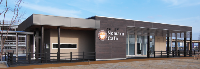 青空の下「NemaruCafe」と白文字で書かれた黒茶色基調の1階建ての建物の写真