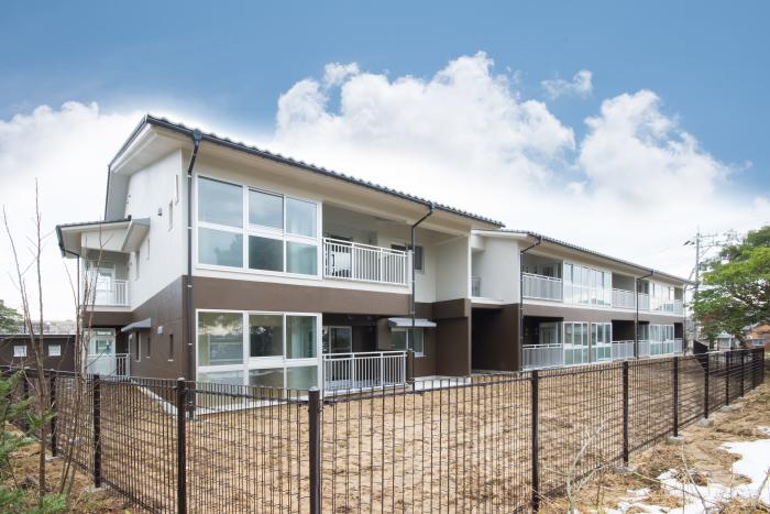 フェンスと芝に囲まれた2階建ての建物の写真