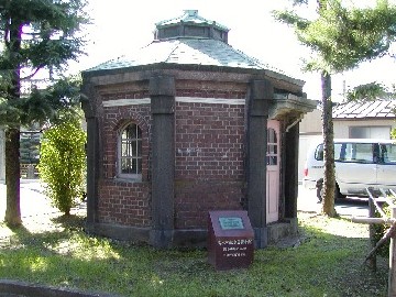 周りに草木などがありそこに茶色いレンガと屋根が緑色で色が少し褪せている一階建ての古びた建物の写真