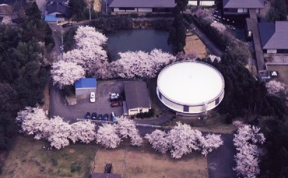 住宅街でドーム型の施設が桜並木に囲まれて存在する伏木配水場を空から俯瞰する写真