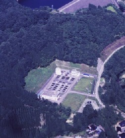 木々に囲まれた白い建物とたくさんの水槽を空から撮影した写真