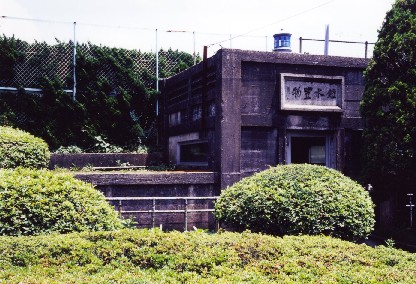 1階建ての建物の周りにフェンスや大きな木、植木などあり建物はすごく古びてコンクリ―トの色が黒茶色に変わってしまっている写真