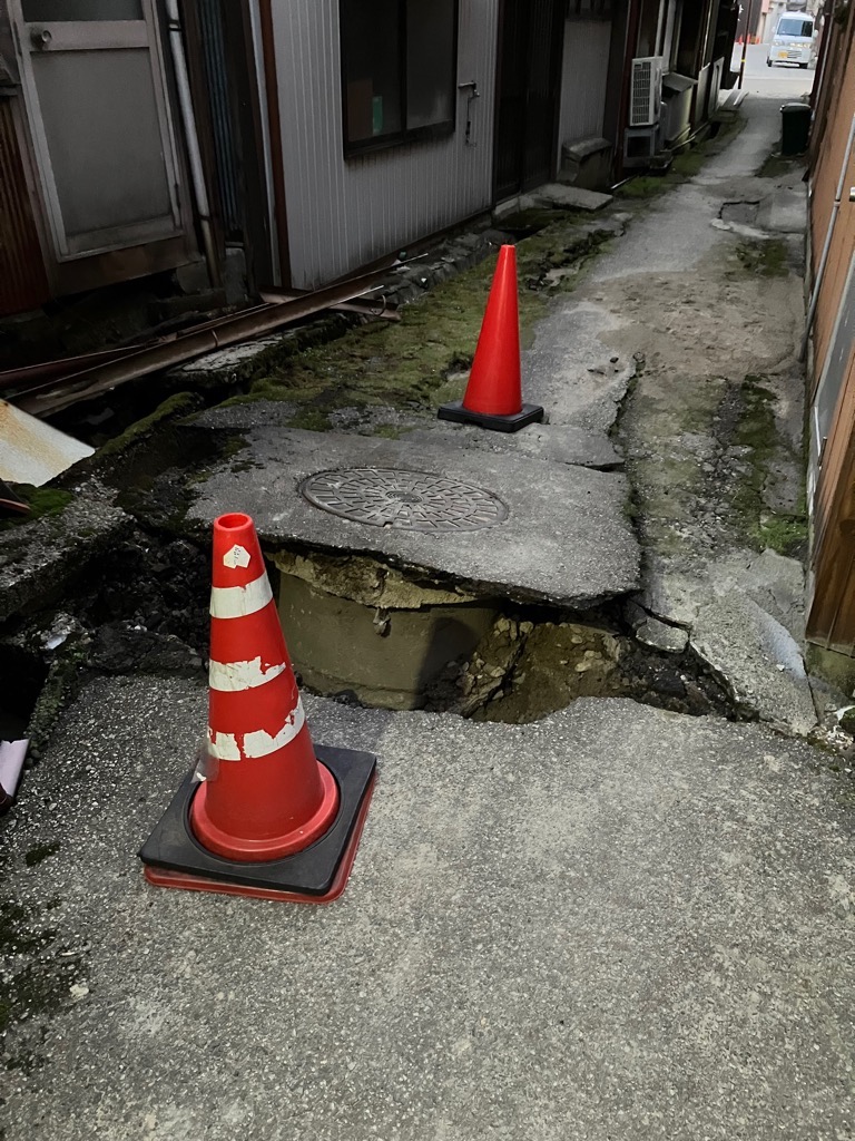 隆起したコンクリートとその周囲に設置された赤い三角コーンの写真