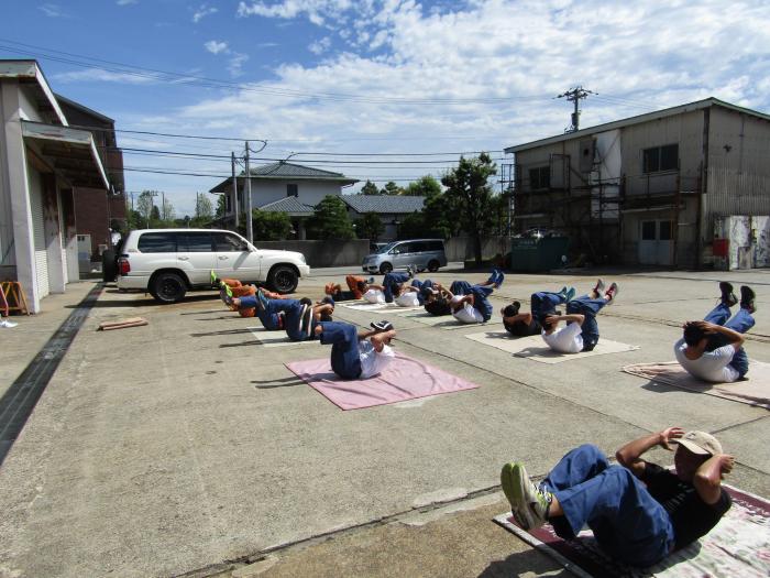 野外で、地面に毛布などを敷いた上でクランチという筋トレをしている14名の男性の様子の写真