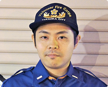 シャッター扉の前で高岡市消防団のキャップをかぶった宮 健太朗さんが正面を向いている様子の写真