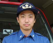 消防車の前で刺繍の入った帽子をかぶった道徳 大介さんが真剣なまなざしでこちらを見ている写真