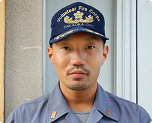 整った髭をたくわえた福島 崇浩さんが高岡市消防団のキャップをかぶり開襟シャツの制服を身に着け正面を向いている様子の写真
