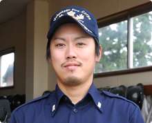 屋内で帽子をかぶり無精ひげを生やした襟にバッジのついたシャツを着ている野原 進さんの写真