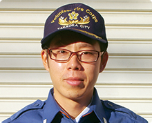 シャッター扉の前で高岡市消防団のキャップをかぶりメガネをかけた中島 徹之さんが正面を向いている様子の写真