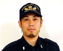 口や顎に髭をたくわえた糀谷 剛さんが高岡市消防団のキャップをかぶり正面を向いている様子の写真