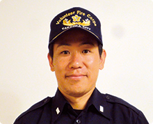 高岡市消防団のキャップと制服を身に着けた健康的な印象の高嶋 渉さんが正面を向いている様子の写真