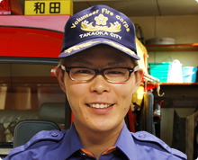 消防車の前で高岡市消防団のキャップをかぶった宮崎 悠希さんが正面を向き笑顔をこちらにむけている様子の写真
