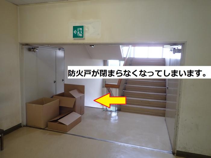 開いている防火扉の前にダンボールが置かれ、「防火扉が閉まらなくなってしまいます。」とテキストで書かれている写真