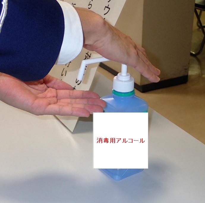 「消毒用アルコール」と書かれた画像のついた青いポンプ式ボトルのポンプを押している写真