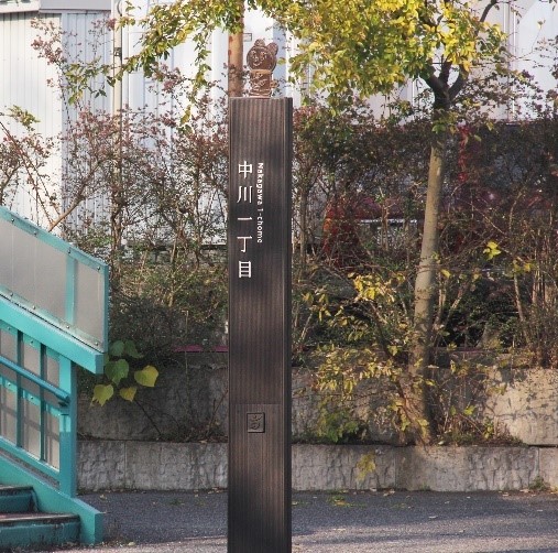 「中川一丁目」と書かれ、上にキャラクターの人形が添えられた案内用のこげ茶色の細長い柱の写真