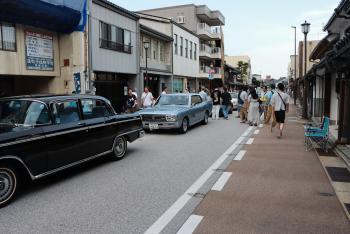 街中の通りに、大型のクラシックカーが数台並んでいる写真