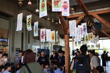 数多くの風鈴と短冊の下に、子連れの女性や、制服を着た幼稚園児たちが集まっている写真