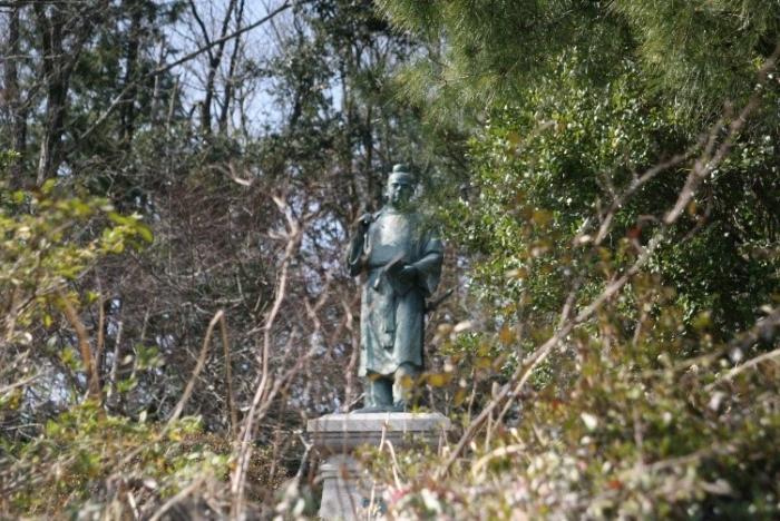 木々が生い茂る中立っている、大伴家持の銅像の写真