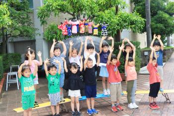 ブロンズ像の前で、子供たちが、手のひらを頭の上に上げ、指を広げて見せている写真