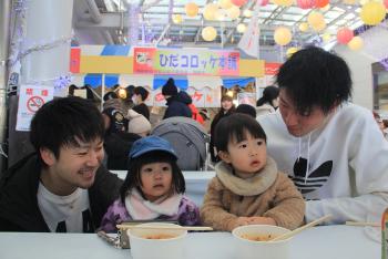 鍋をお椀に入れて食べる子供と、その姿を笑顔で見守る大人の写真