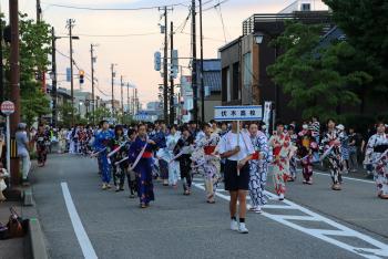 伏木高校のプラカードを持った半ズボンの男子児童の後ろを、浴衣を着た女子生徒たちが並んで歩いている写真