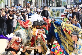 様々な色の布地でで彩られた獅子が、観客の前で舞っている写真