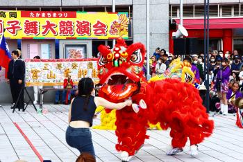 真っ赤な体と極彩色の顔をした台湾風の獅子が、「獅子舞大競演会」と書かれた看板の前で舞っている写真