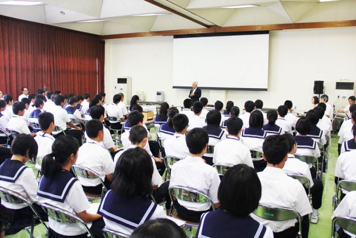 二上まなび交流館第1研修室にて、一番前で立って講演を行なっている高岡市長の話を聞く、高岡市内12の中学校の生徒会の生徒達の写真